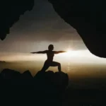 A person performing yoga poses on a mountainside at sunset