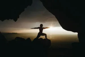 A person performing yoga poses on a mountainside at sunset