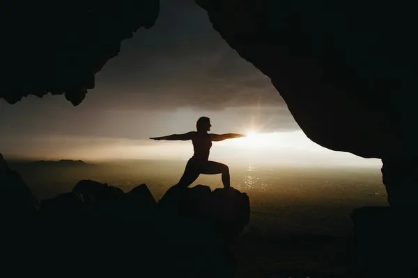 A person performing yoga poses on a mountainside at sunset