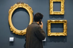 A man on his cell phone at a museum looking at pictureless frames.